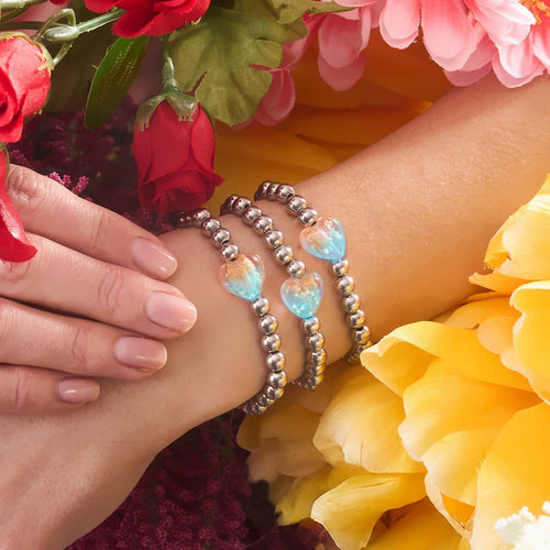 Gilded Pink Glowing Heart Essence Bracelets with silver-plated beads and luminous pink heart charms worn on wrist surrounded by flowers by NOGU